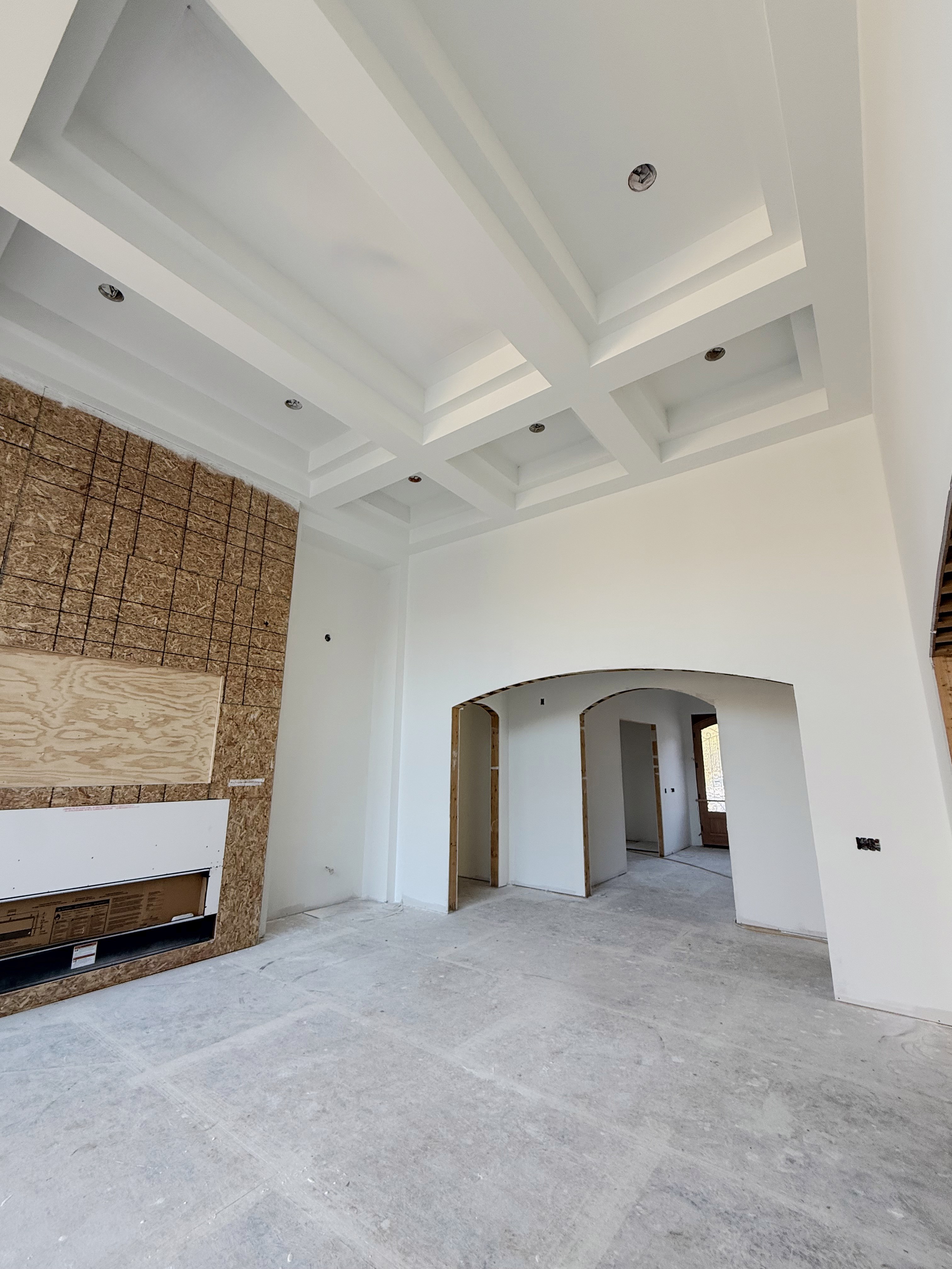New build: two-story great room with a coffered ceiling, looking toward arched drywall doorways